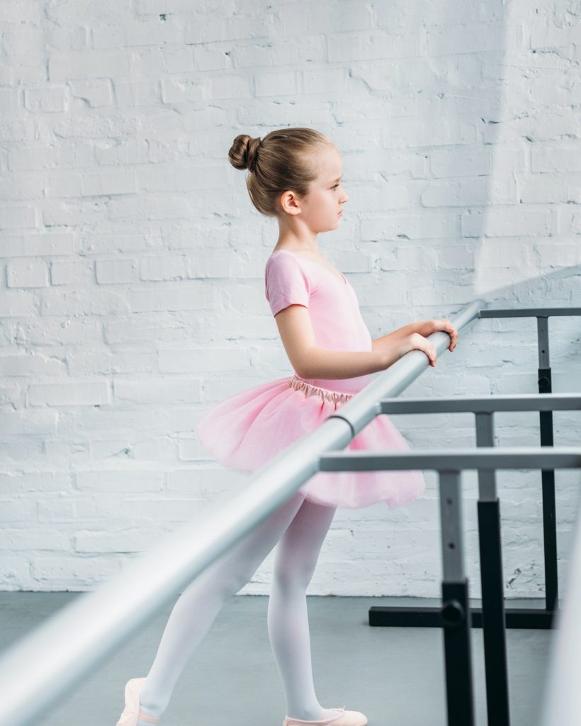 side view of beautiful little ballerina practicing ballet in studio